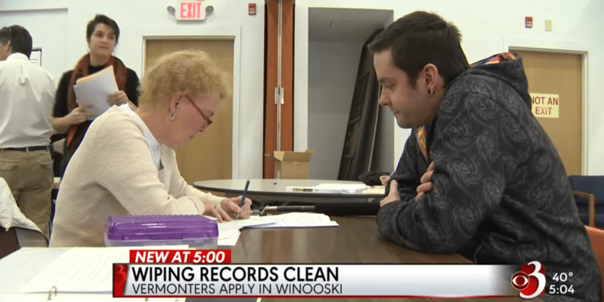 a local news feature of the expungement clinic. two people sit across from each other at a table filling out paperwork