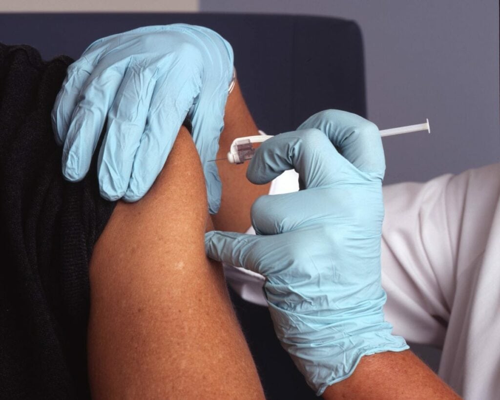 close up image of a person with gloved hands injecting a vaccine into someone's upper arm