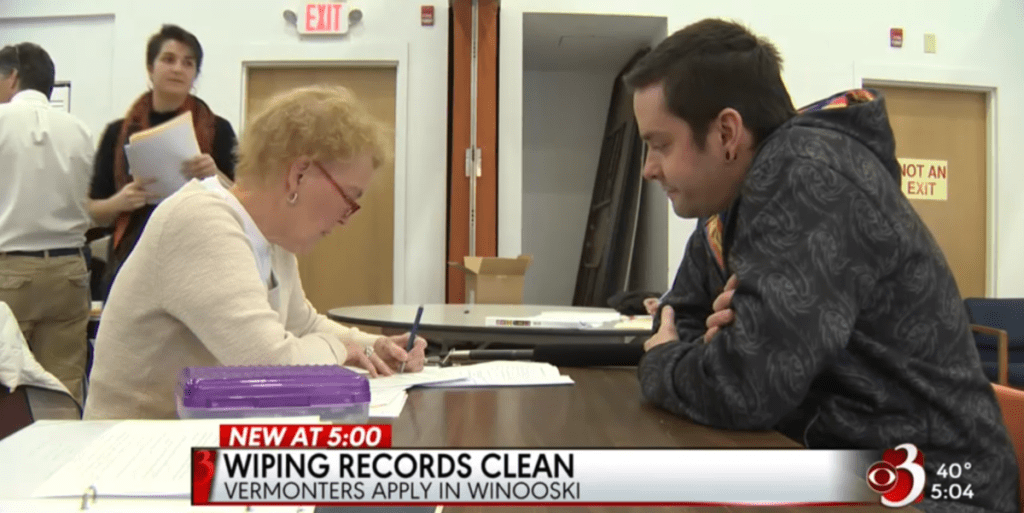 a local news feature of the expungement clinic. two people sit across from each other at a table filling out paperwork