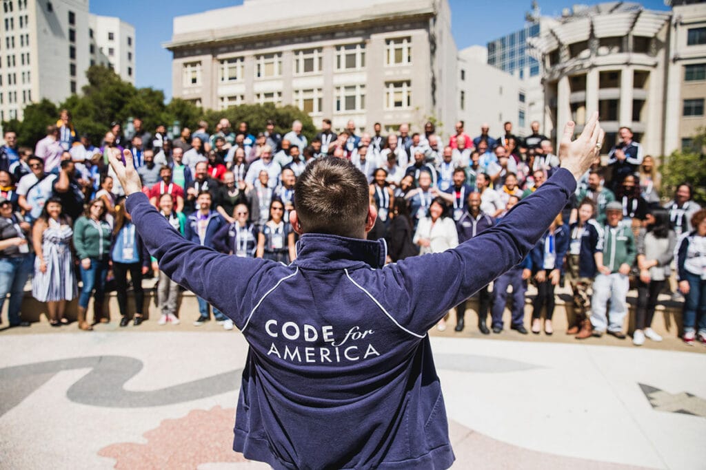 A man raises his arms as a large group of Summit attendees in the background get ready to pose for a group photo
